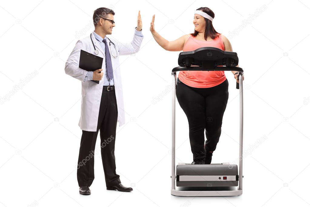 Full length profile shot of a doctor high-fiving an overweight woman exercising on a treadmill isolated on white background