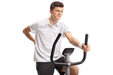 Bir egzersiz bisikleti binme ve sırt ağrısı beyaz arka plan üzerinde izole yaşayan genç