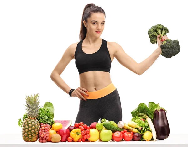 健身妇女与西兰花哑铃在桌子后面的水果和蔬菜隔离在白色背景 — 图库照片