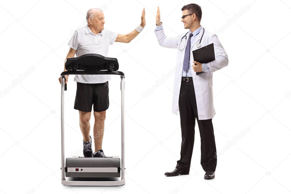 Full length profile shot of a senior walking on a treadmill and high-fiving a doctor isolated on white background