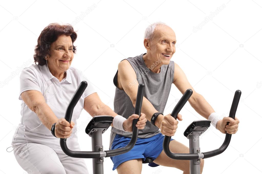 Seniors exercising on stationary bikes isolated on white background