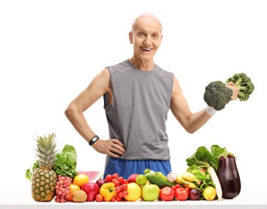 Yaşlı adam ile meyve ve sebze beyaz arka plan üzerinde izole bir masanın arkasında bir brokoli dumbbell tutarak
