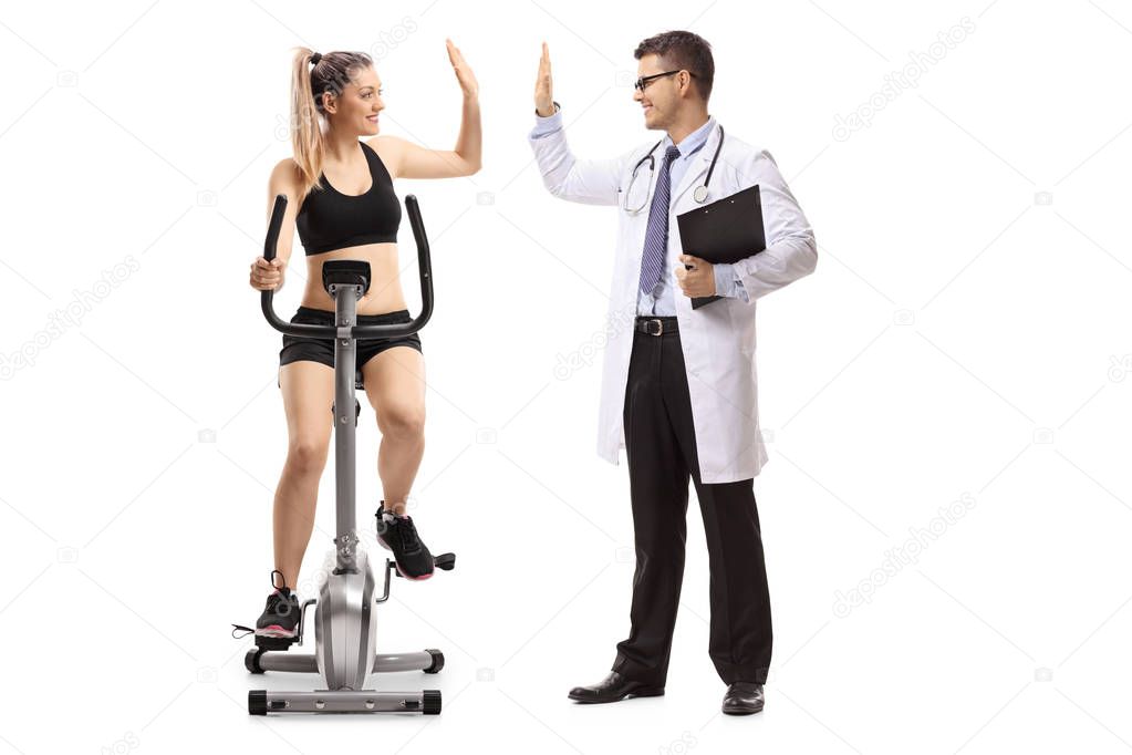 Young woman exercising on a stationary bike and high-fiving a doctor isolated on white background