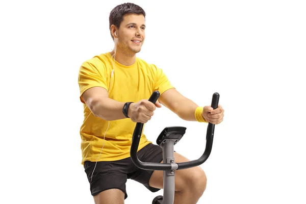 戴着耳机的年轻人在白色背景的固定自行车上锻炼 — 图库照片
