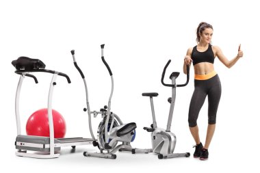 Tam uzunlukta egzersiz makineleri tarafından ayakta ve beyaz arka plan üzerinde izole jest bir başparmak yapma bir fitness kız portresi