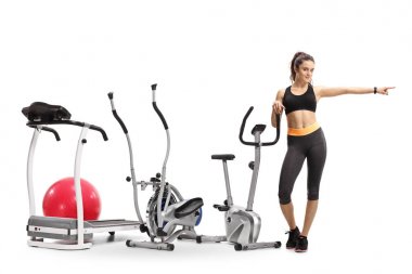 Beyaz arka plan üzerinde izole bir fitness kadın işaret egzersiz makineleri ile tam uzunlukta portresi