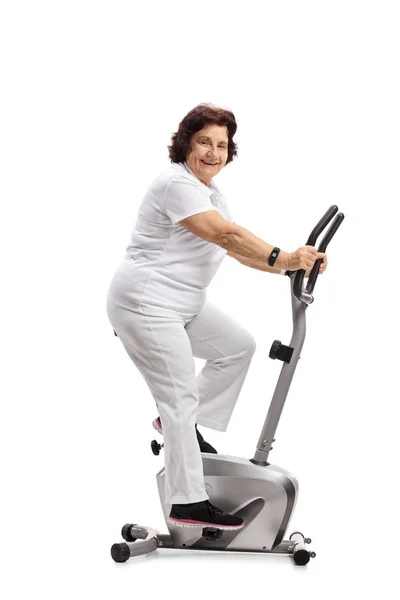 老年妇女在固定的自行车上锻炼 看着在白色背景下隔离的相机 — 图库照片