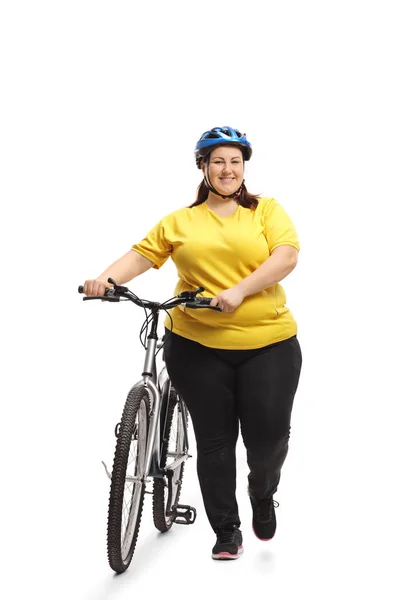 Full length portrait of an overweight woman with a bicycle walking towards the camera isolated on white background
