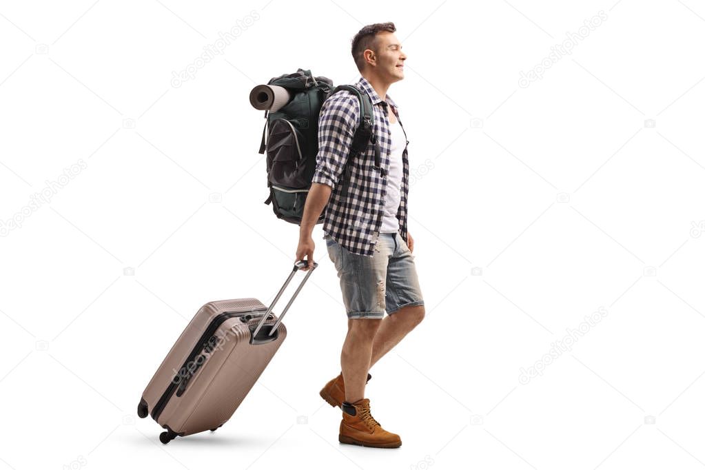 Full length profile shot of a tourist with a backpack and a suitcase walking isolated on white background