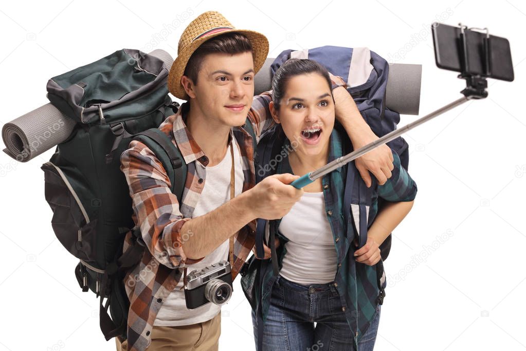 Teenage tourists with backpacks taking a selfie with a stick isolated on white background