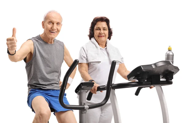 老人骑着一辆健身自行车 在白色背景的跑步机上与一位年长的妇女做拇指标记 — 图库照片