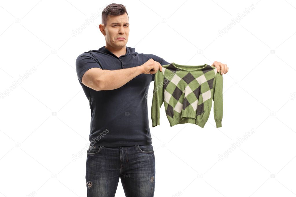 Upset young man holding a shrunken blouse isolated on white background