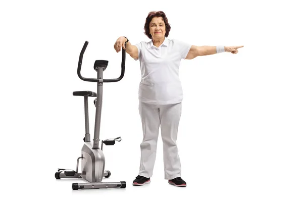 Full Length Portrait Elderly Woman Leaning Exercise Bike Pointing Isolated — Stock Photo, Image