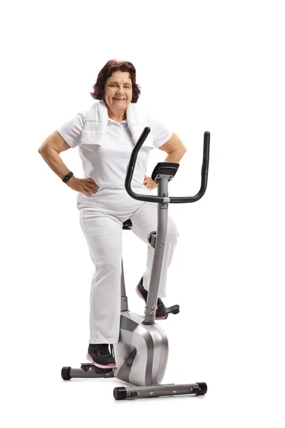 Elderly woman sitting on an exercise bike isolated on white background