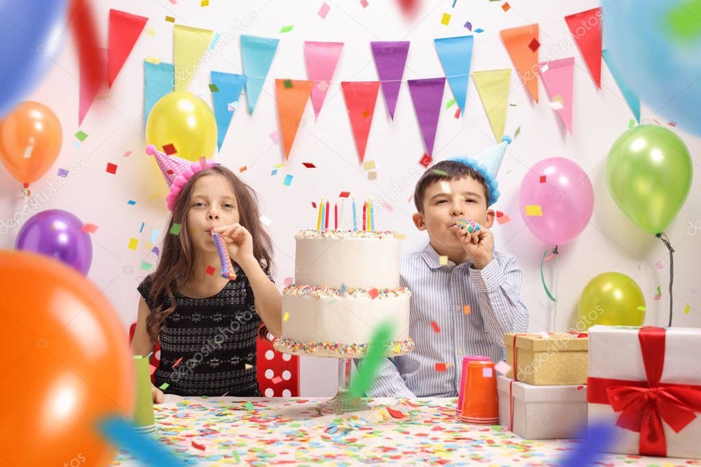 Little girl and a little boy with party horns and a cake celebrating a birthday