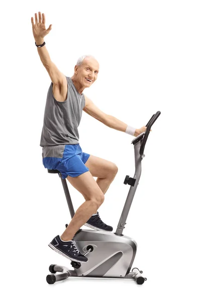 Elderly Man Exercising Stationary Bike Waving Camera Isolated White Background — Stock Photo, Image