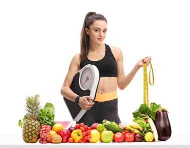 Bir ağırlık ölçek ve beyaz arka plan üzerinde izole sebze ve meyve ile bir masanın arkasında bir ölçüm bandı tutan fitness kadın