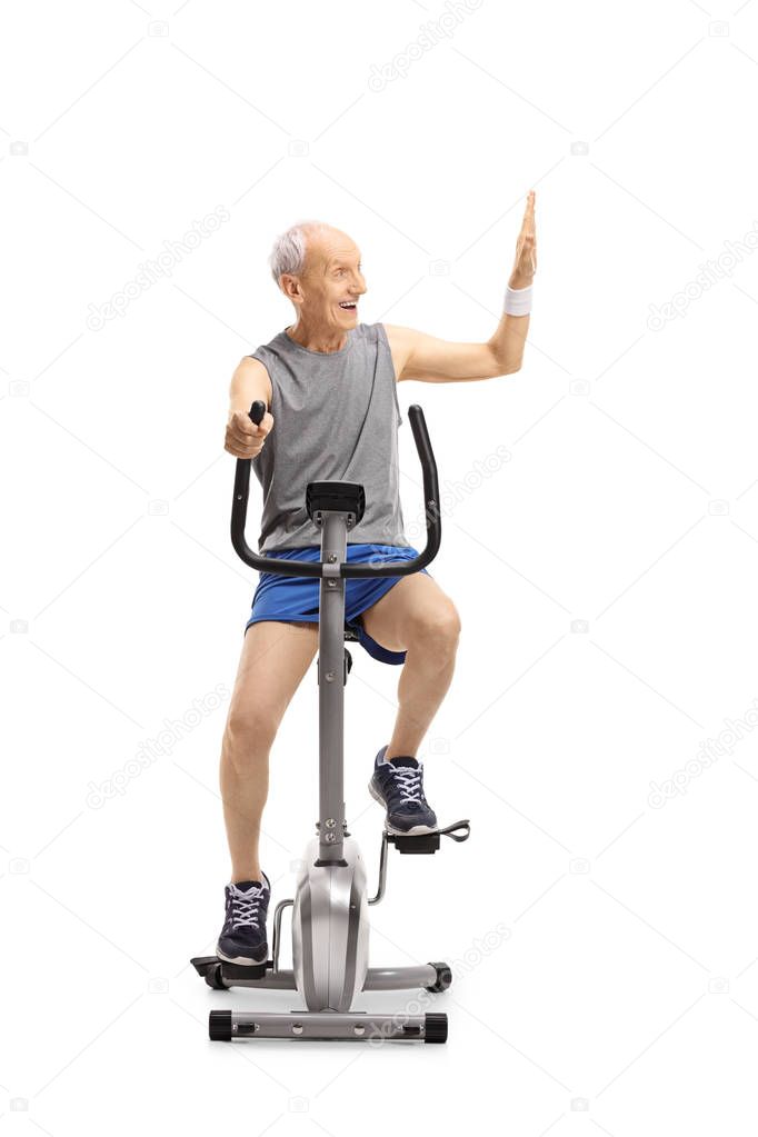 Senior exercising on a stationary bike making a high-five gesture isolated on white background