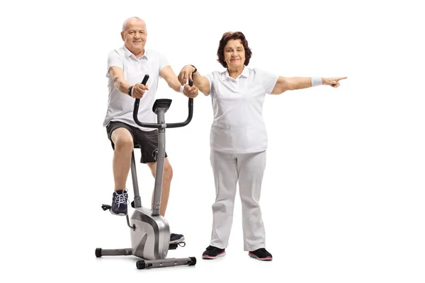 Mature Man Riding Stationary Bike Mature Woman Pointing Isolated White — Stock Photo, Image