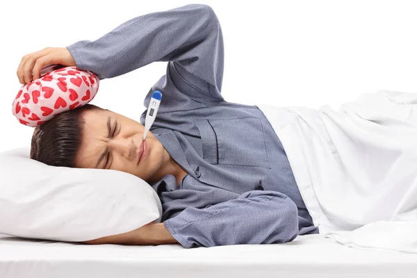 生病的青少年躺在床上拿着一个 Icepack 在他的头和一个温度计在他的嘴孤立的白色背景 — 图库照片