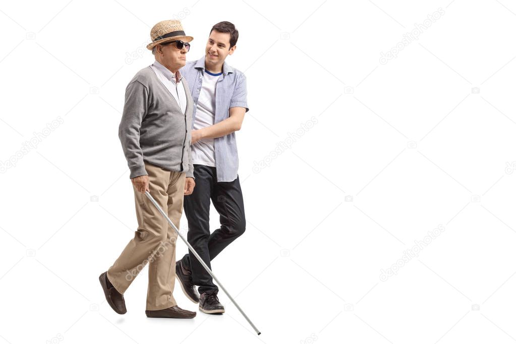 Full length profile shot a blind mature man walking with the help of a young man isolated on white background