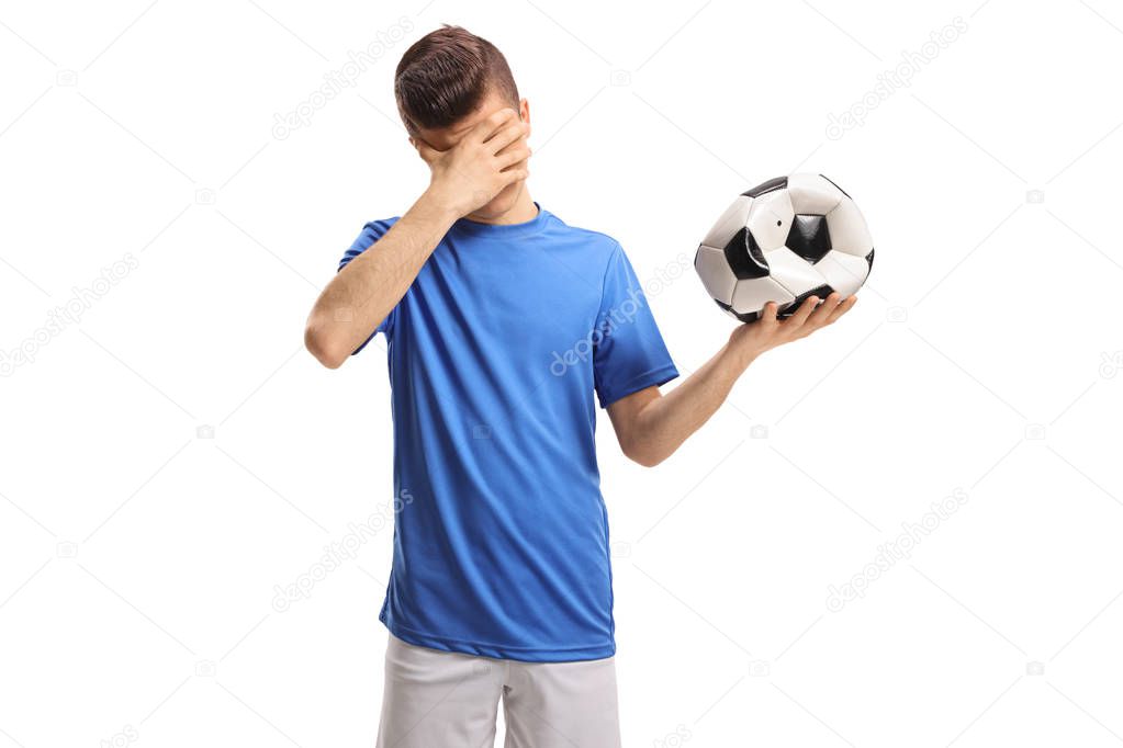Teenage soccer player with a deflated football holding his head in disbelief isolated on white background