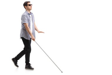 Beyaz arka planda sopayla yürüyen kör bir gencin tam boy profil fotoğrafı.
