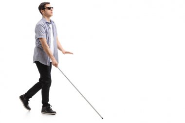 Full length profile shot of a blind young man with a cane walking isolated on white background