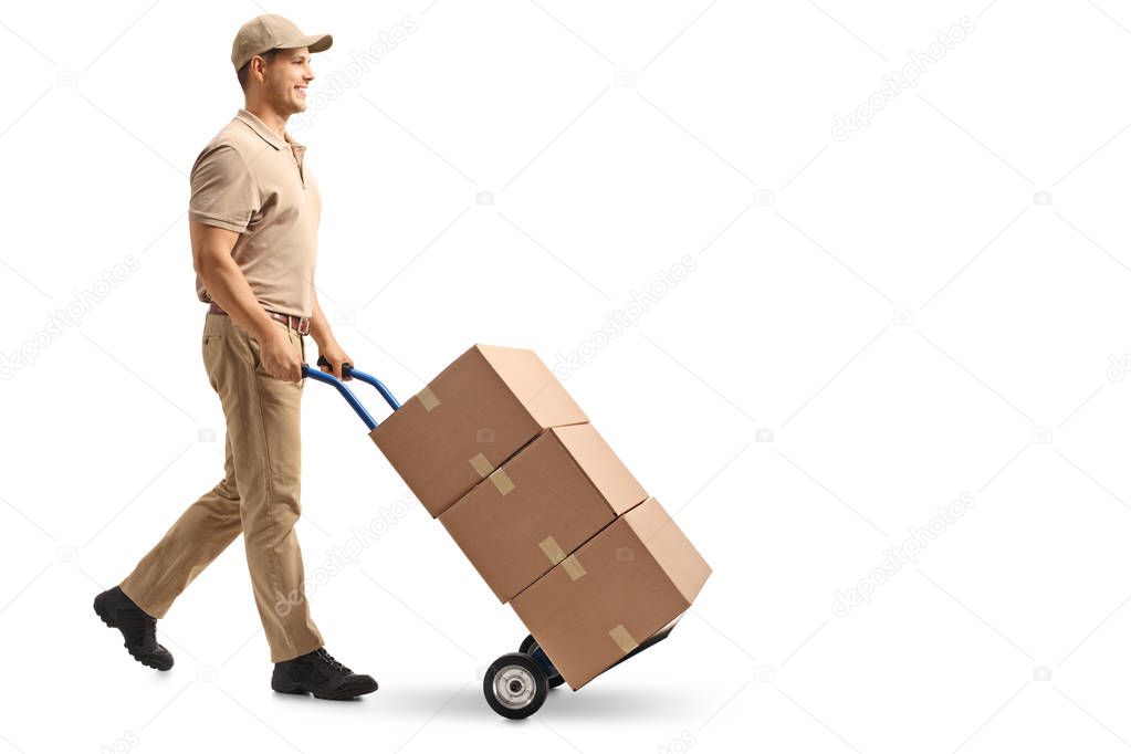Full length profile shot of a delivery guy pushing a hand truck with boxes isolated on white background
