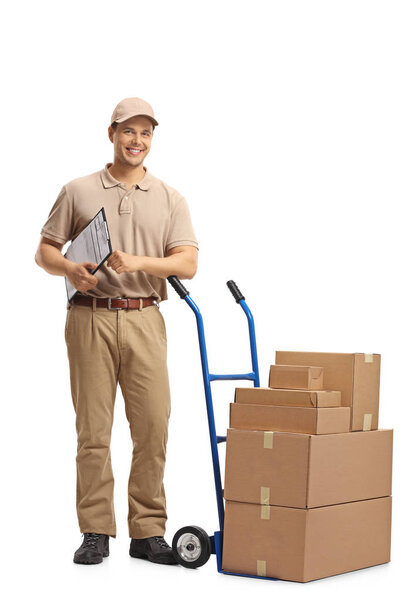 Full length portrait of a delivery man with a clipboard leaning on a hand truck with a stack of boxes isolated on white background