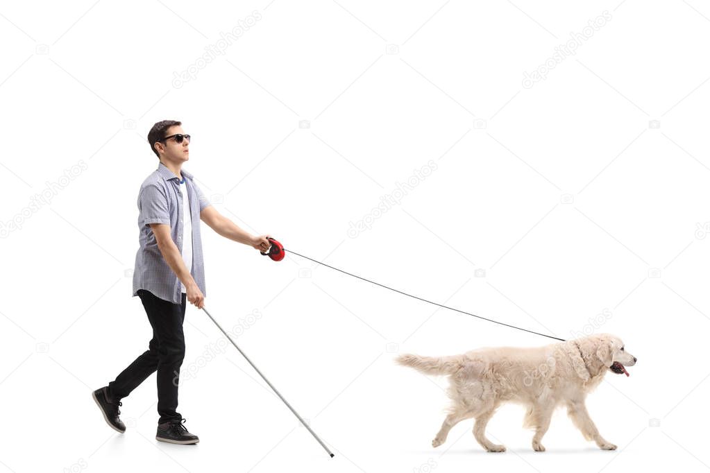 Full length profile shot of a blind young man walking with the help of a dog isolated on white background