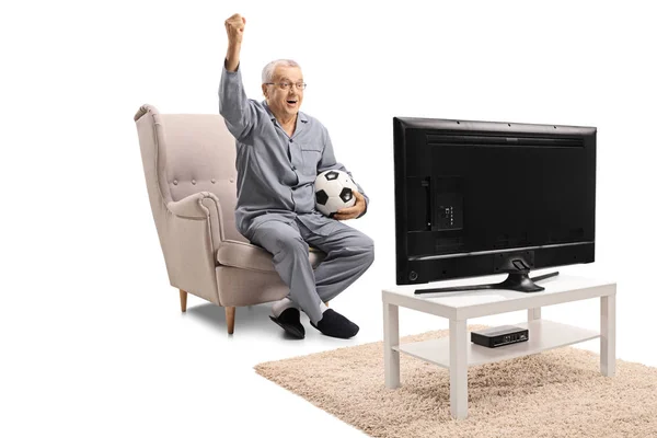 快乐的成熟男子穿着睡衣坐在扶手椅上看足球电视和握住他的手在白色背景上孤立 — 图库照片
