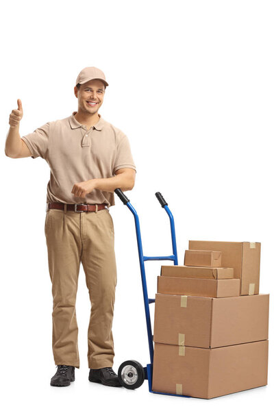 Full length portrait of a delivery man with a hand truck loaded with boxes making a thumb up sign isolated on white background