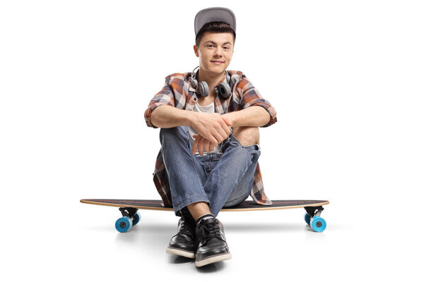 Подросток, сидящий на длинной доске и смотрящий на камеру, изолированную на белом фоне
