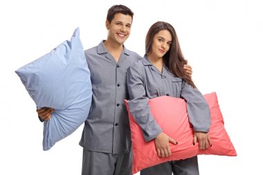 Genç çift yastık tutarak ve beyaz arka plan üzerinde izole kamera bakarak pijama