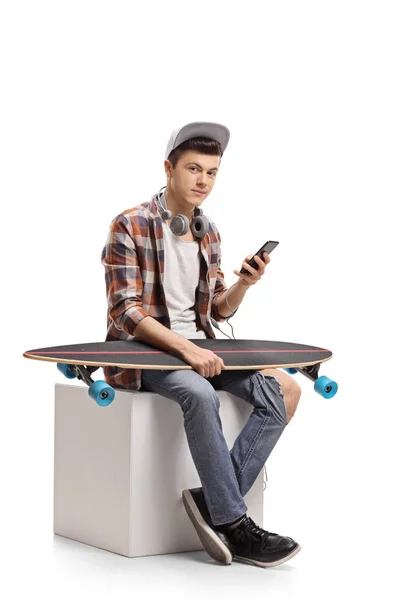 携帯電話と白い背景で隔離のキューブの上に座ってロングボード 代のスケーター — ストック写真