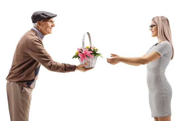 Elderly man giving a basket with flowers to a young woman — Stock Photo, Image