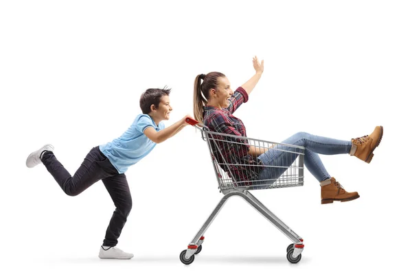 Menino empurrando sua irmã adolescente em um carrinho de compras — Fotografia de Stock