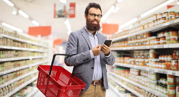 쇼핑 바구니와 휴대 전화를 들고 서 있는 수염을 한 남자 — 스톡 사진