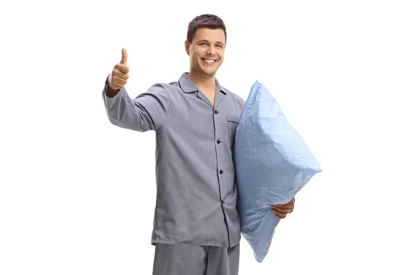 Χαμογελώντας άνθρωπος με πιτζάμες κρατώντας ένα μαξιλάρι και κάνοντας έναν αντίχειρα μέχρι si — Φωτογραφία Αρχείου