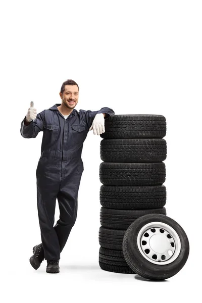 Mecánico apoyado en una pila de neumáticos y mostrando un pulgar hacia arriba signo — Foto de Stock