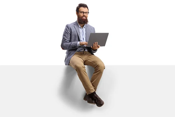 Man met baard werkend op een laptop en zittend op een banner — Stockfoto