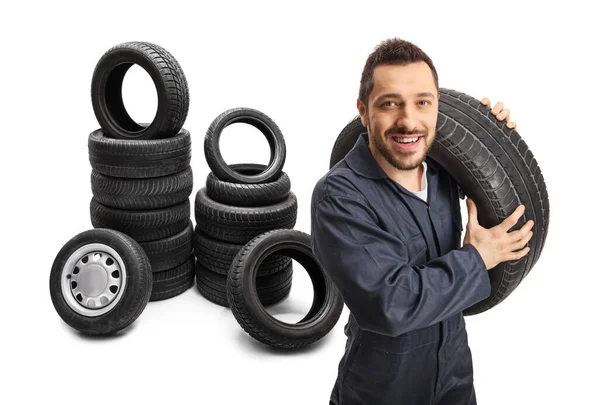 Mecánico llevando un neumático de vehículo con montones de neumáticos detrás de él — Foto de Stock