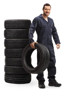 Bir yığın lastiğin yanında duran oto tamircisi