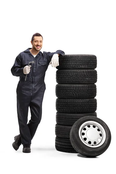 Mechanic holding a lug wrench and leaning on a pile of car tires — Stock Photo, Image