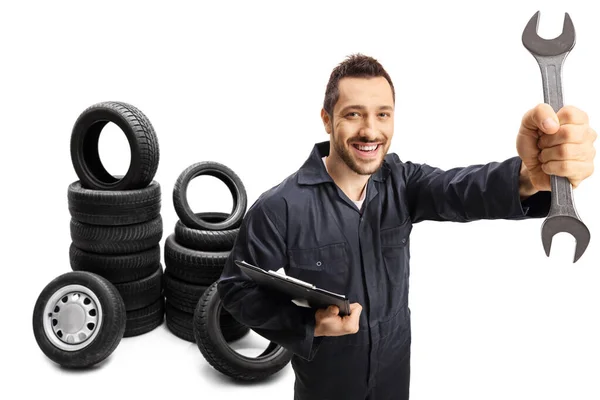 Auto mechanic holding a wrench with car tires in the back — Stock Photo, Image