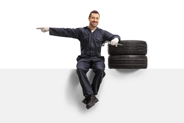Auto monteur zit op een paneel met banden en een moersleutel en poi — Stockfoto