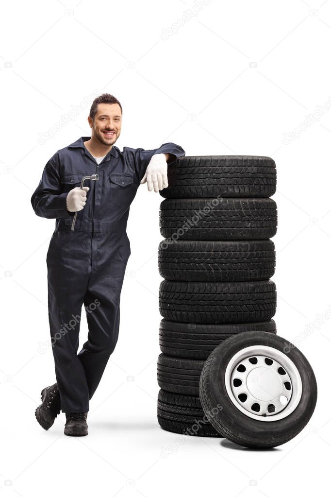 Mechanic holding a lug wrench and leaning on a pile of car tires