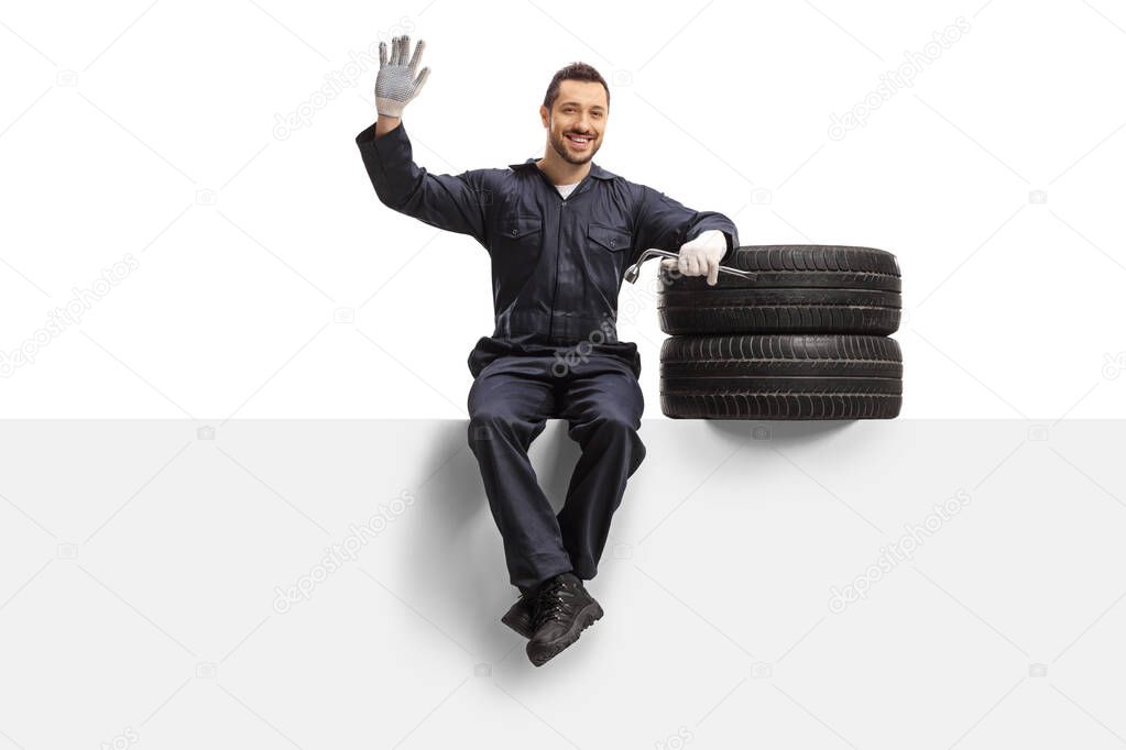 Auto mechanic sitting on a panel with tires and a wrench and wav