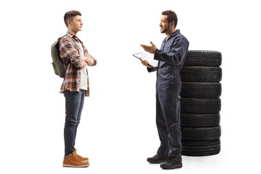 Araba lastiklerinin yanında duran ve bir erkekle konuşan oto tamircisi.